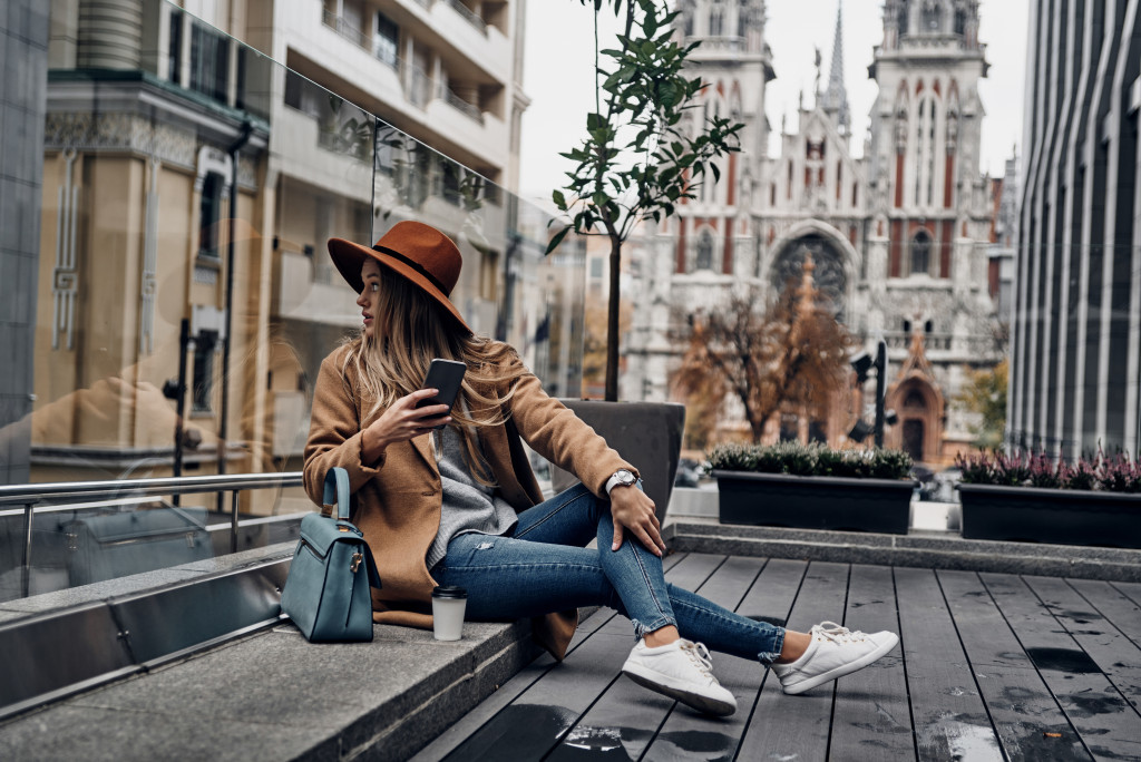 Young woman sitting on a low bench while wearing chic clothing.