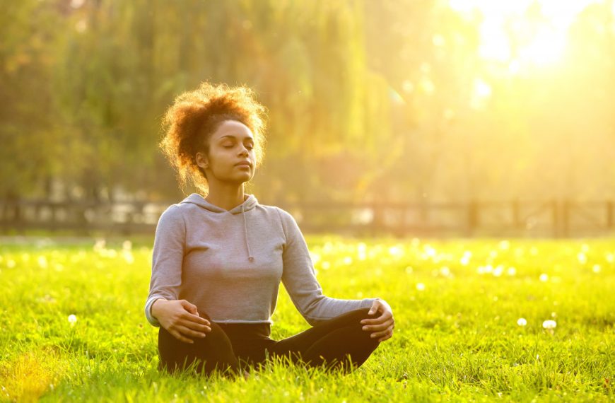 woman sitting in a grass patch meditating under the sun